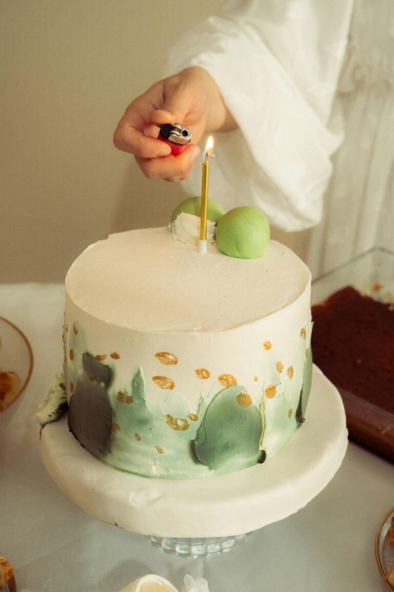 A stylish cake adorned with green designs, topped with a candle, being lit for celebration.