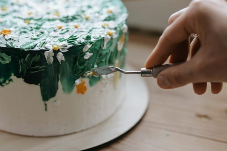 Close-up of a hand artistically decorating a cake with floral motifs using a palette knife.