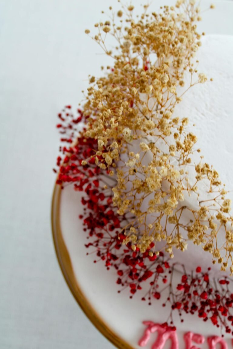 Decorative white cake adorned with red and golden dried flowers on a plate.